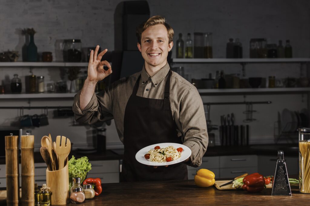 mid shot chef holding plate with pasta making ok sign